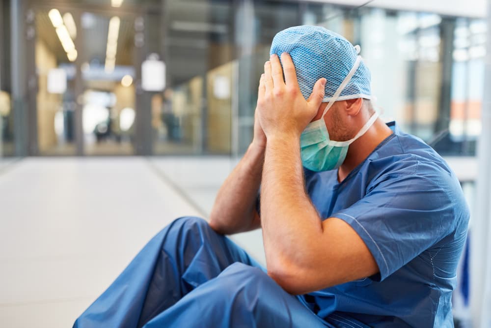 Desperate surgeon in blue surgical clothes with hands in front of the face