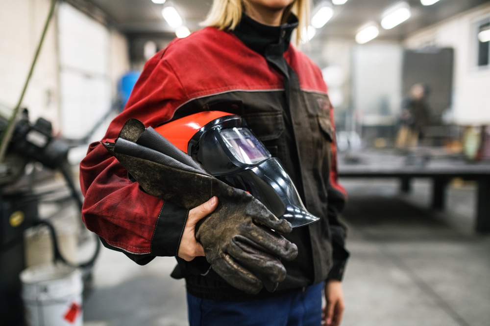 Construction worker holding a welding helmet and protective gloves, emphasizing the importance of proper eye protection on job sites.