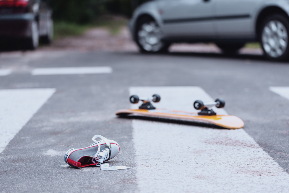 Skateboard and shoe left in a crosswalk after a vehicle strike, showing the aftermath of a pedestrian accident.