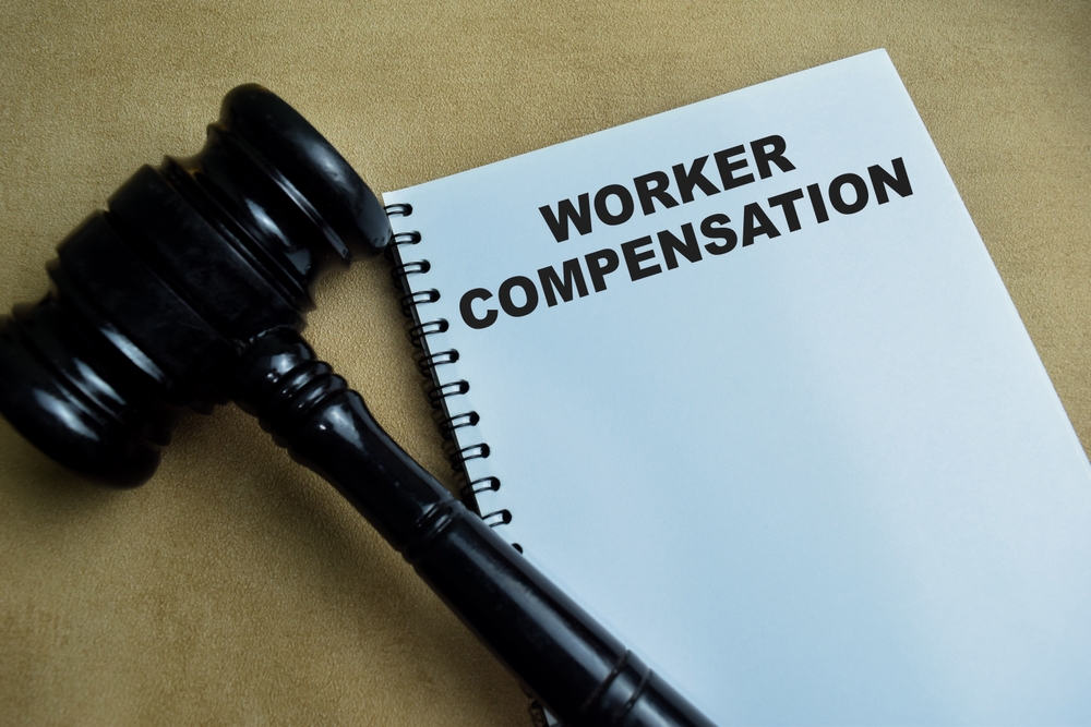 Workers&rsquo; compensation notebook with judge&rsquo;s gavel representing legal implications of OSHA reporting and injury documentation