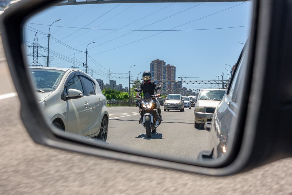 The reflection of a motorcycle in the left side mirror of a car traveling in traffic