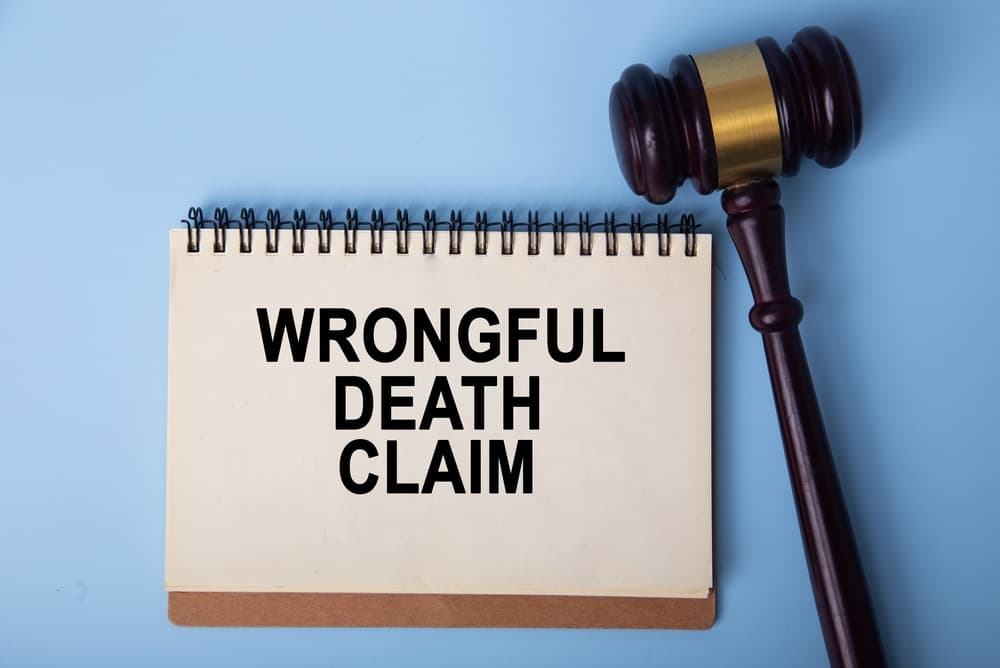 Notepad displaying wrongful death claim next to a wooden gavel on blue background