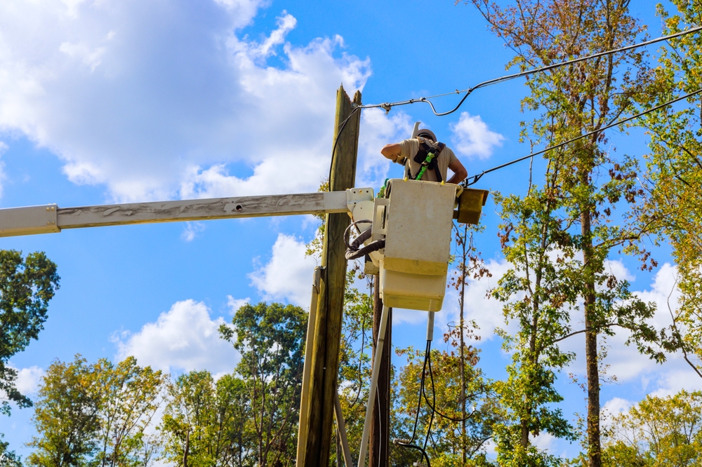 A lineman in a cherry picker performs maintenance on a line from a utility pole