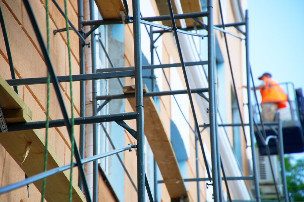 Workman using ladder and scaffolding to repair face of building